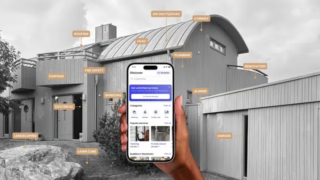 En hand håller upp en mobil med BuddyPro-appen framför ett hus märkt med tjänster som tak, el, vvs och målning.